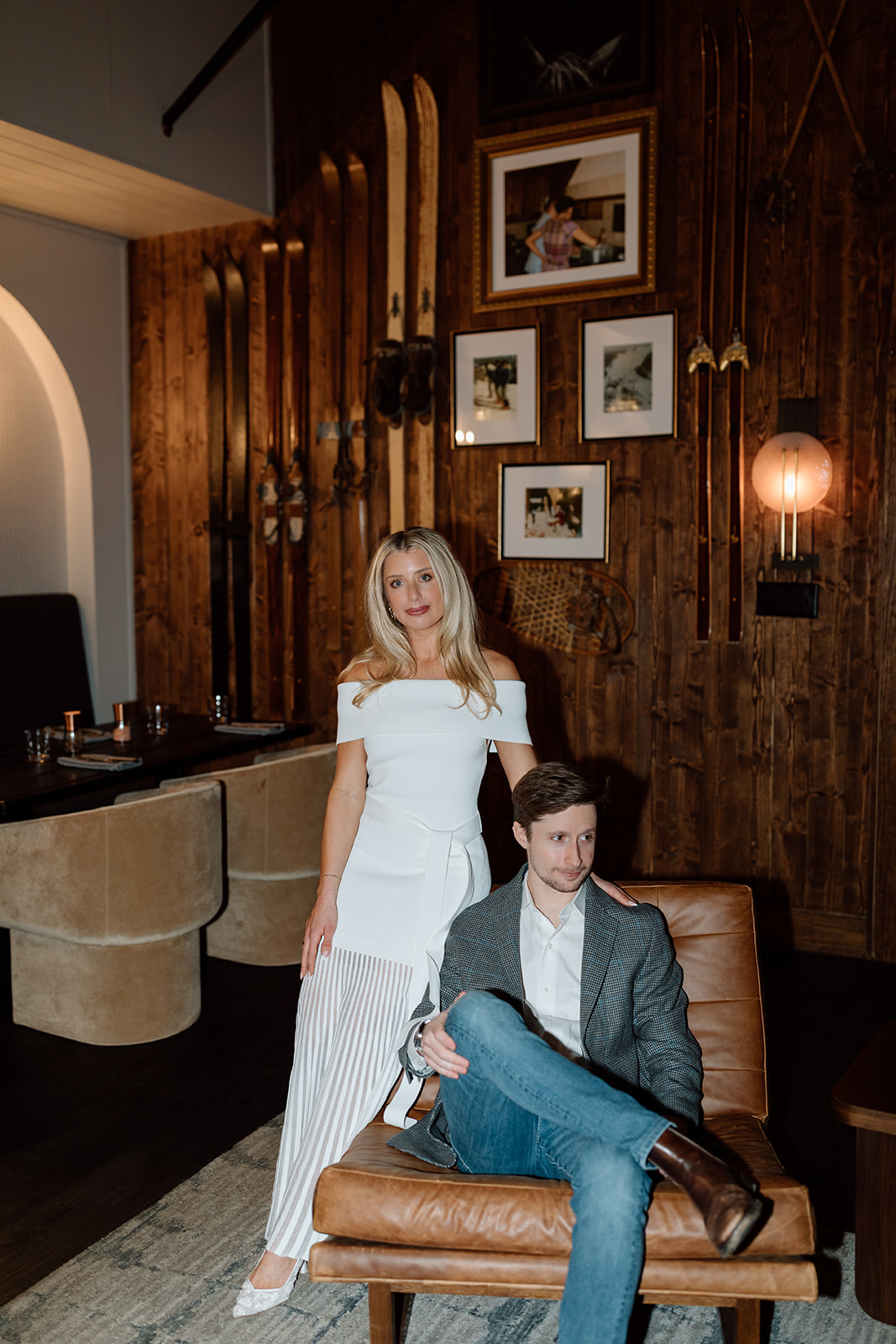 A couple poses in the lodge in front of the vintage ski gallery wall